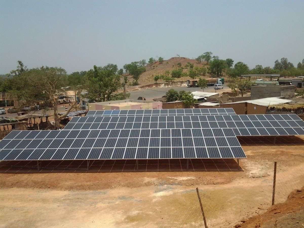 A ground-mounted solar array in a walled compound with hills behind it