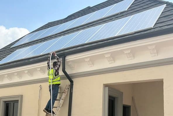 An Endlos Energy technician on a ladder running cable to a rooftop solar array on an Abuja home